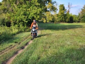 A boy riding a KTM bike in an open field filled with plants